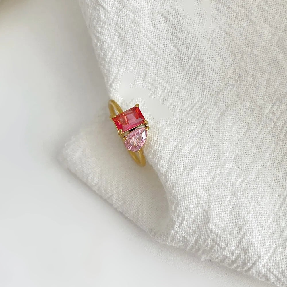 Anel com pedra retangular e gota dourado sobre tecido branco