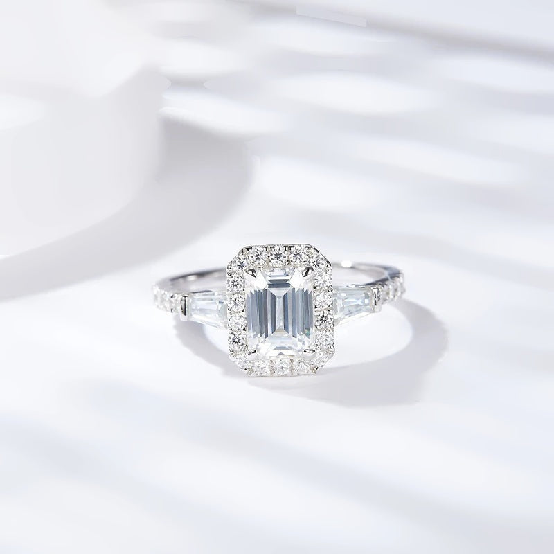 Anel de moissanite corte esmeralda com halo sobre tecido claro