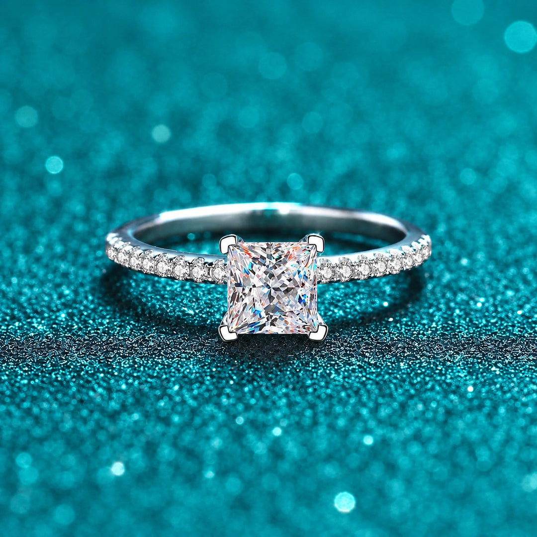 Anel Solitário Princesa de Moissanite com Aro Cravejado em prata 925 sobre fundo verde com brilho