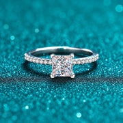 Anel Solitário Princesa de Moissanite com Aro Cravejado em prata 925 sobre fundo verde com brilho