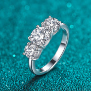 Anel Três Pedras Redondas de Moissanite 2 ct ou 4 ct em prata 925 sobre fundo verde com brilho