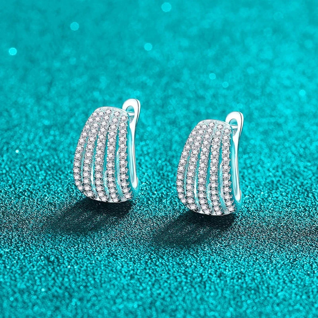 Par de argolas largas cravejadas de moissanite sobre fundo verde-água