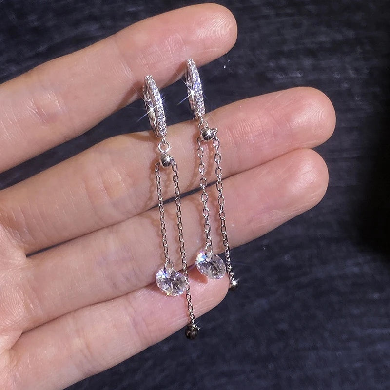 Brincos com corrente e moissanite apoiados na mão