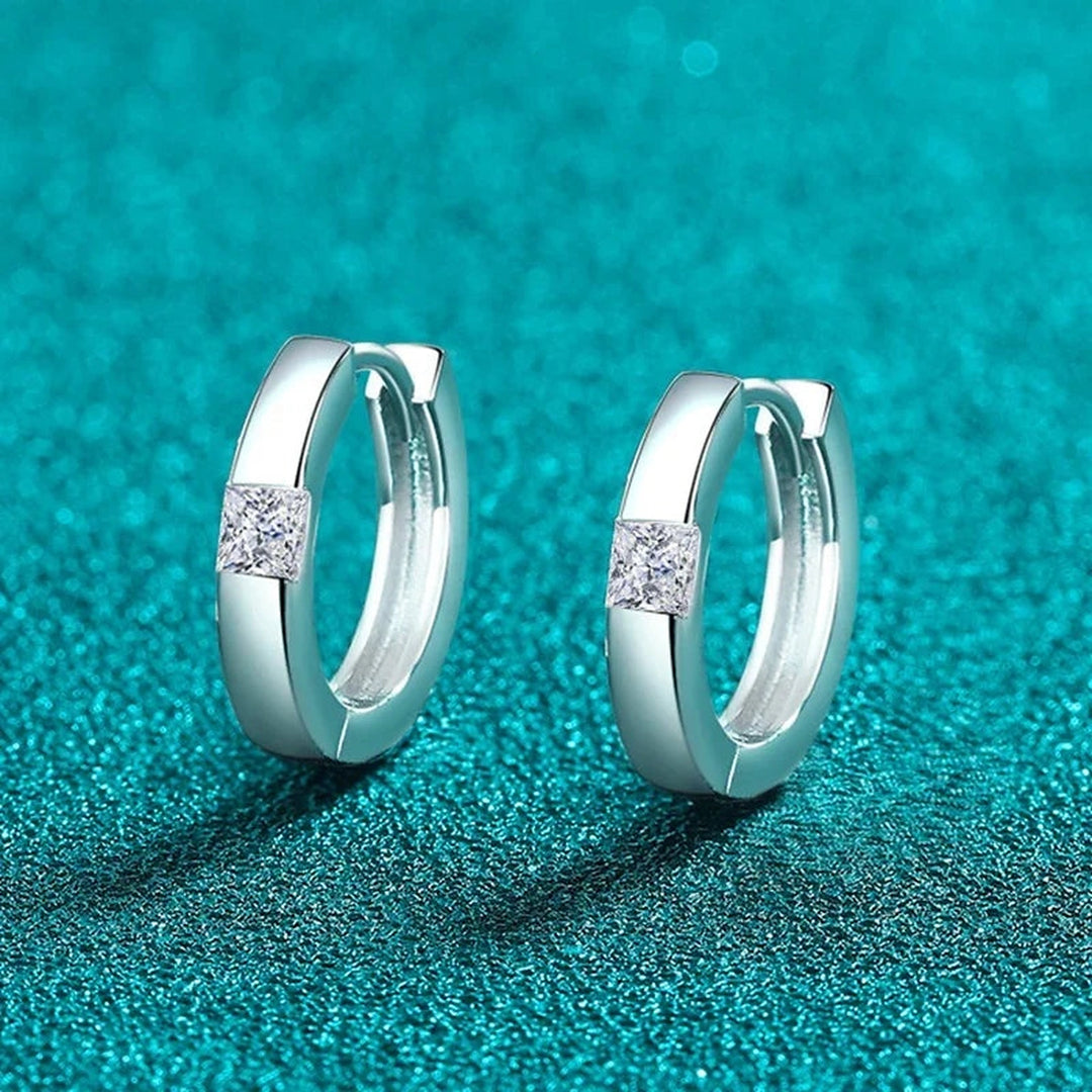 Par de argolinhas com moissanite quadrada sobre fundo verde-água