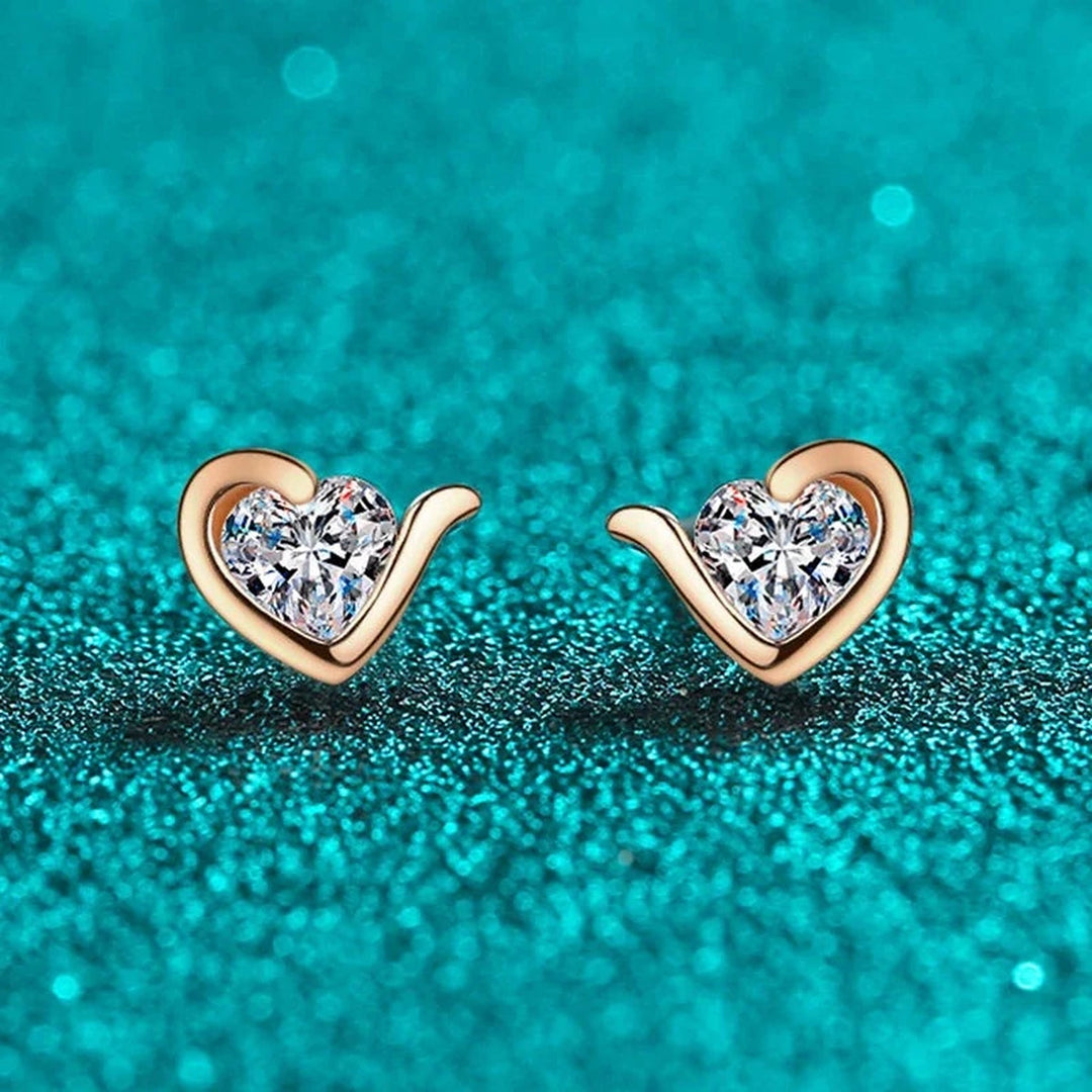 Par de brincos coração de moissanite em ouro rosé sobre fundo verde-água