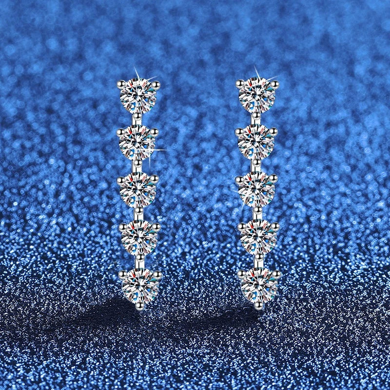 Par de brincos com cinco moissanites alinhadas sobre fundo azul brilhante