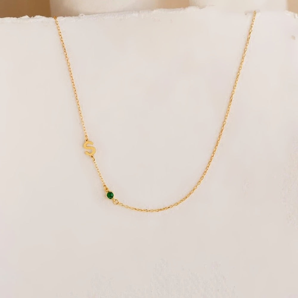 Colar com inicial lateral e pedra verde dourado sobre papel branco