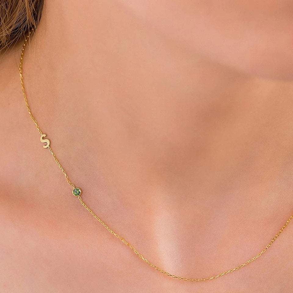 Colar assimétrico com inicial S e pedra verde dourado no colo