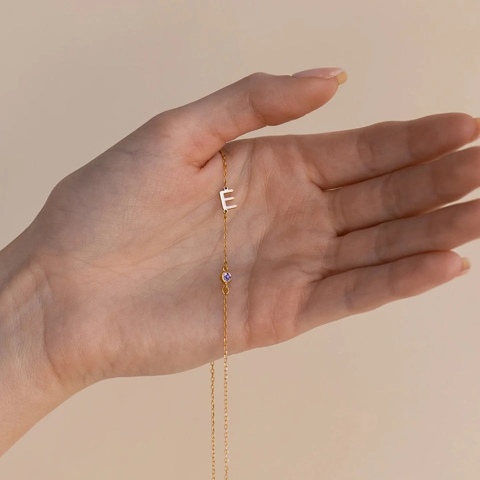 Colar com inicial E e pedra do mês dourado na mão