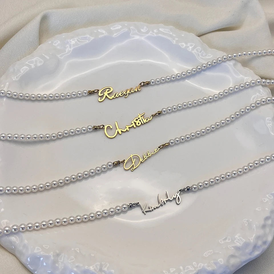 Quatro colares de pérolas com nomes dourados e prata sobre prato branco