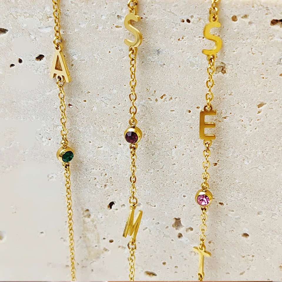 Detalhe das letras douradas e pedras do mês dos colares de iniciais