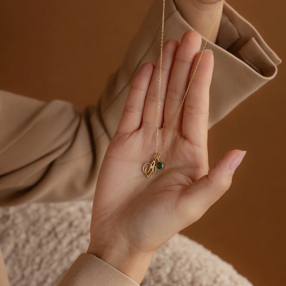 Colar com inicial cursiva e pedra verde dourado na palma da mão