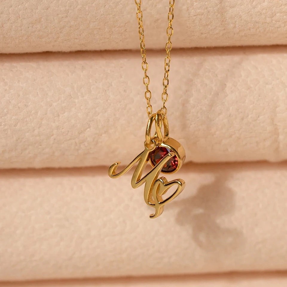 Colar com inicial M e pedra do mês dourado sobre tecido rosado