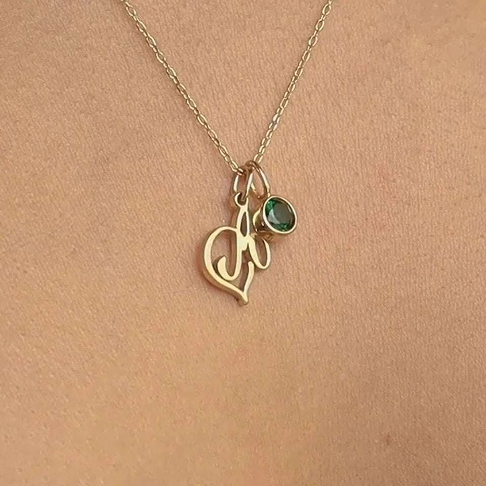 Detalhe da letra cursiva com coração e pedra verde do colar com inicial