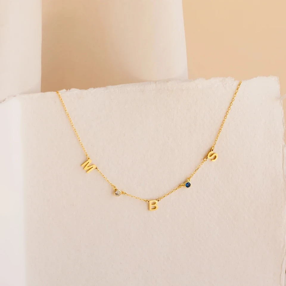Colar com letras M B S e pedras do mês dourado sobre papel