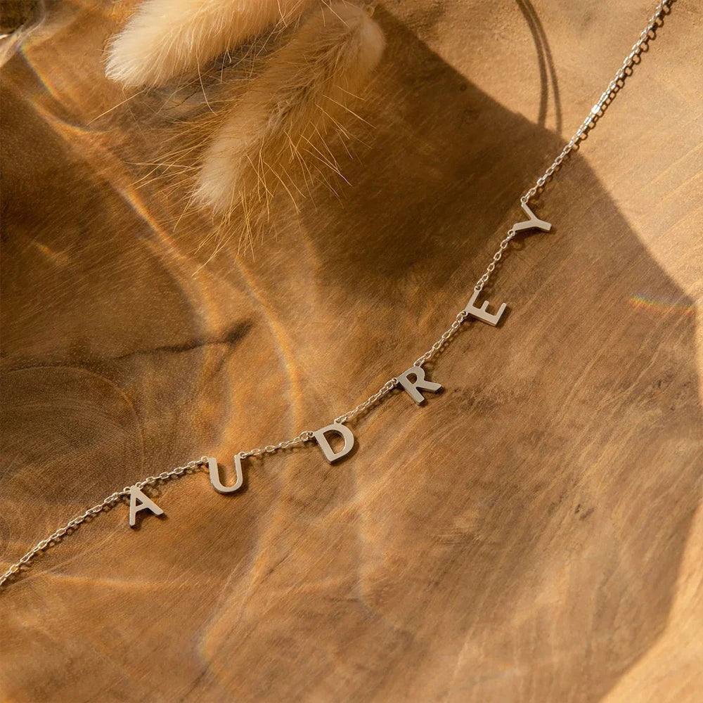 Colar com letras soltas formando o nome Audrey sobre madeira