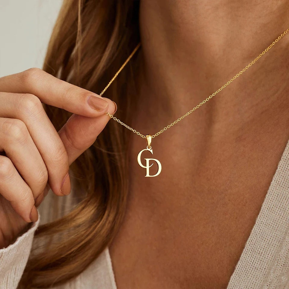 Mão segurando colar monograma com iniciais C e D dourado