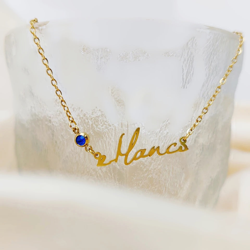 Colar com nome dourado e pedra azul apoiado em vidro