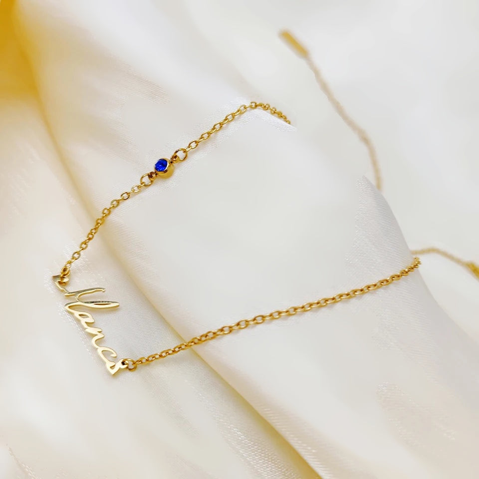 Colar com nome dourado e pedra azul sobre tecido