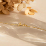 Pulseira com nome dourada em corrente fina sobre tecido claro
