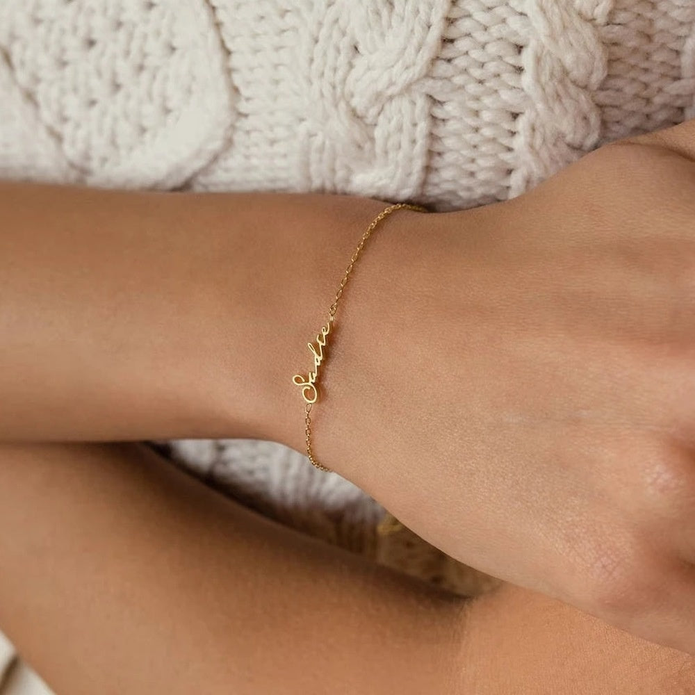 Pulseira com nome dourada no pulso com suéter branco