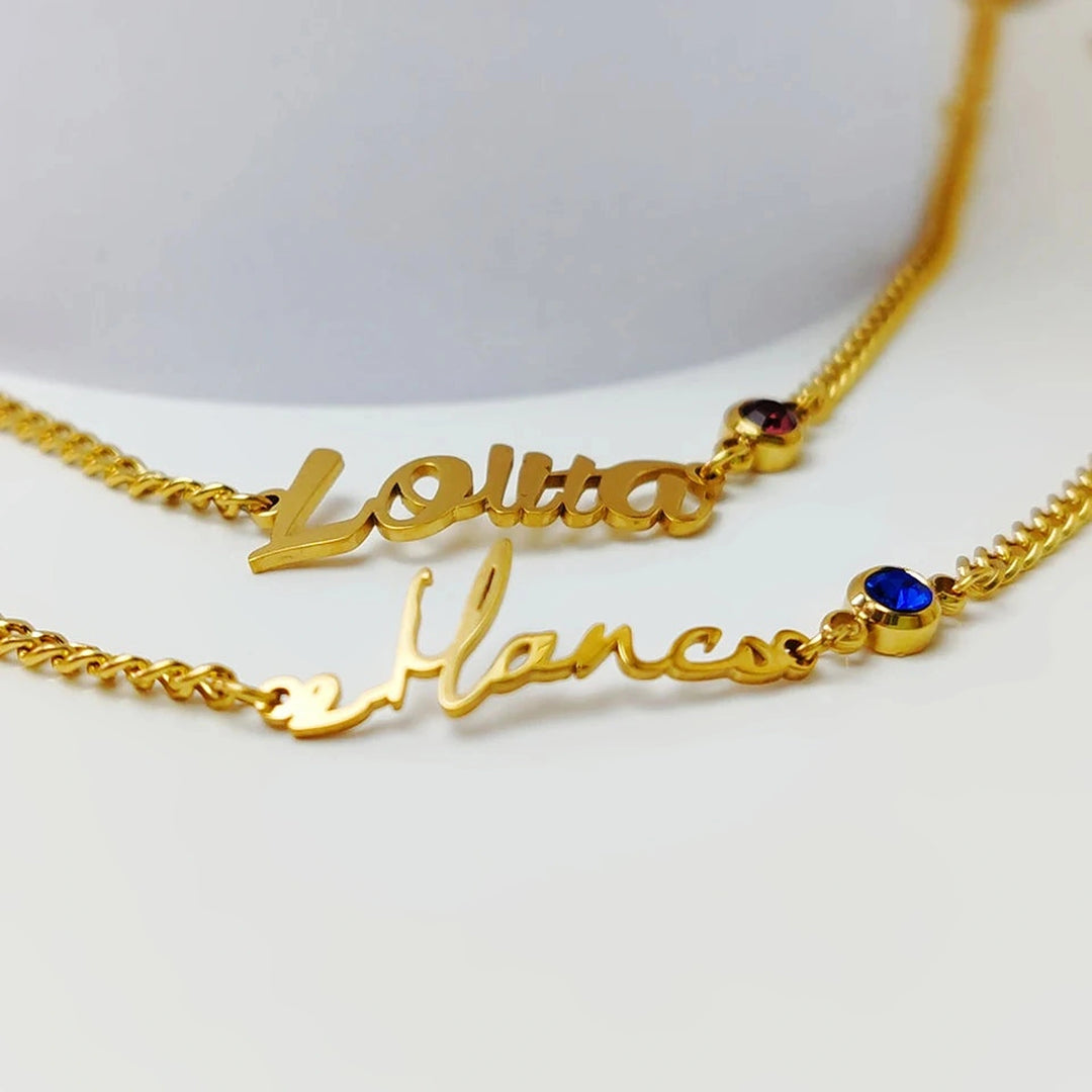 Duas pulseiras groumet douradas com nome e pedra do mês vermelha e azul