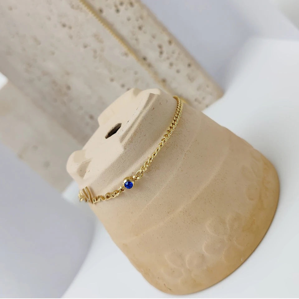 Pulseira dourada com nome e pedra azul sobre peça de cerâmica
