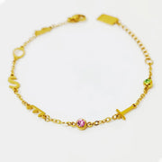 Pulseira com iniciais douradas e pedras do mês rosa e verde sobre fundo branco