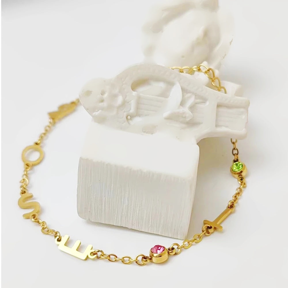 Pulseira com letras e pedras do mês sobre peça decorativa branca