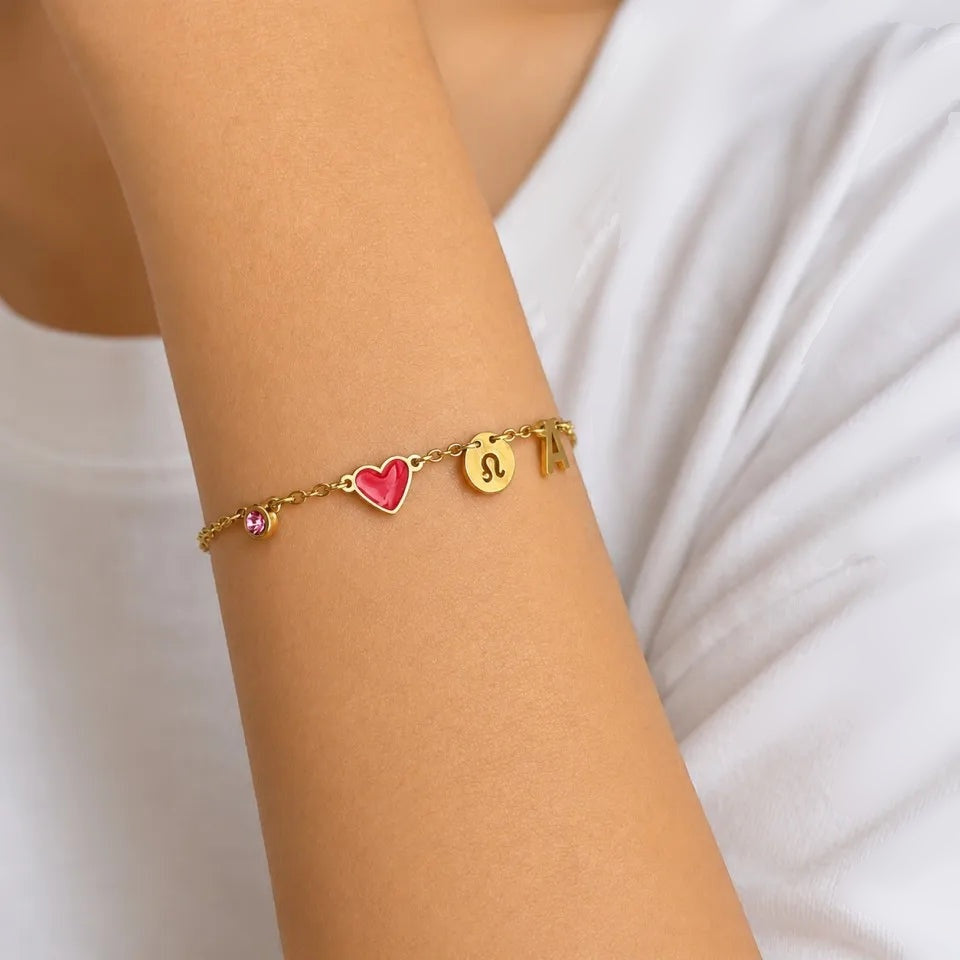 Pulseira com coração vermelho, signo de leão e inicial no pulso