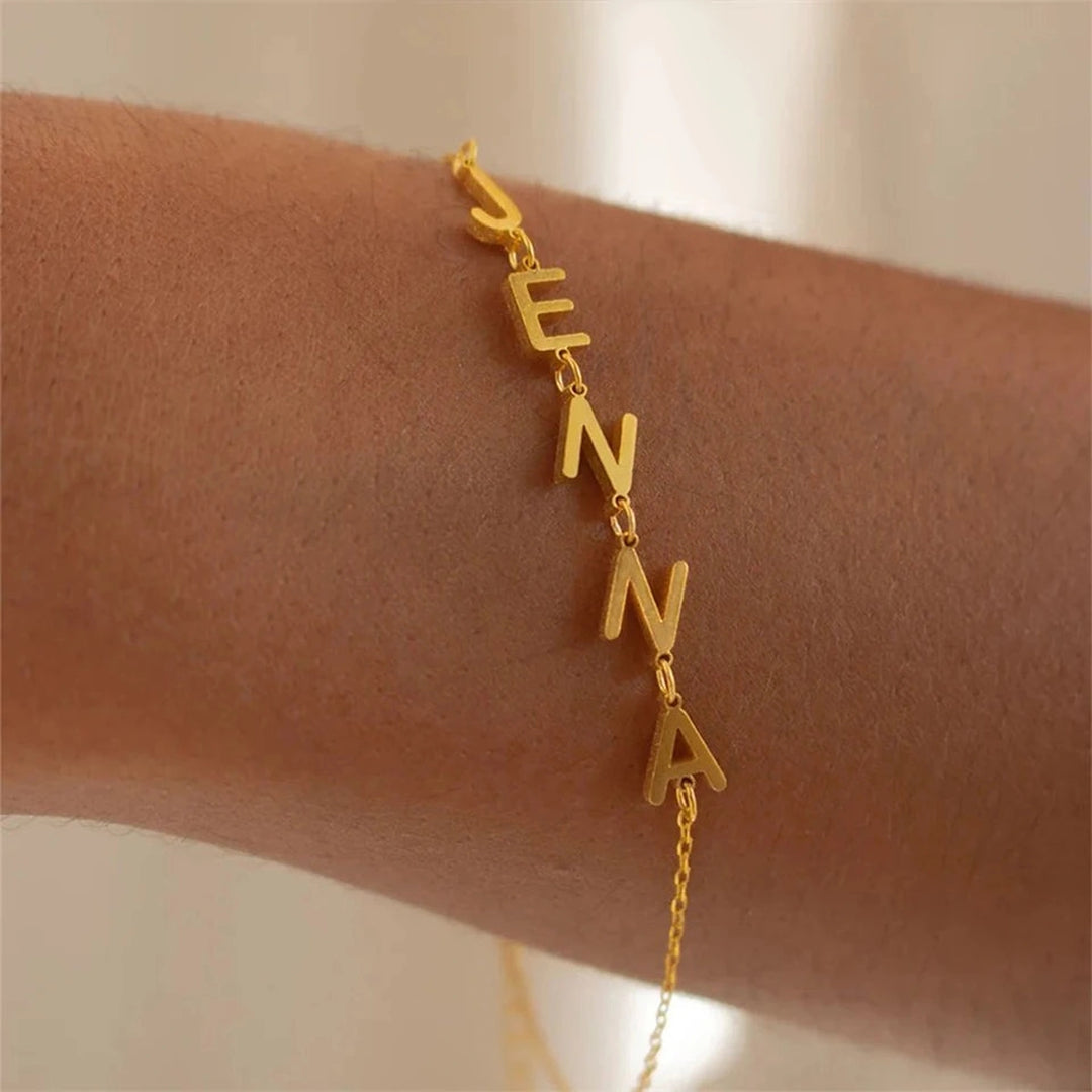 Pulseira com letras laterais douradas formando o nome Jenna no pulso