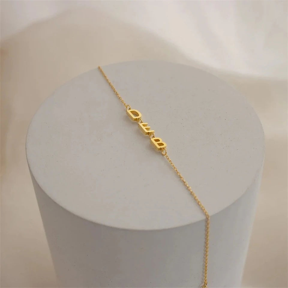 Pulseira personalizada com três letras laterais douradas sobre pedestal
