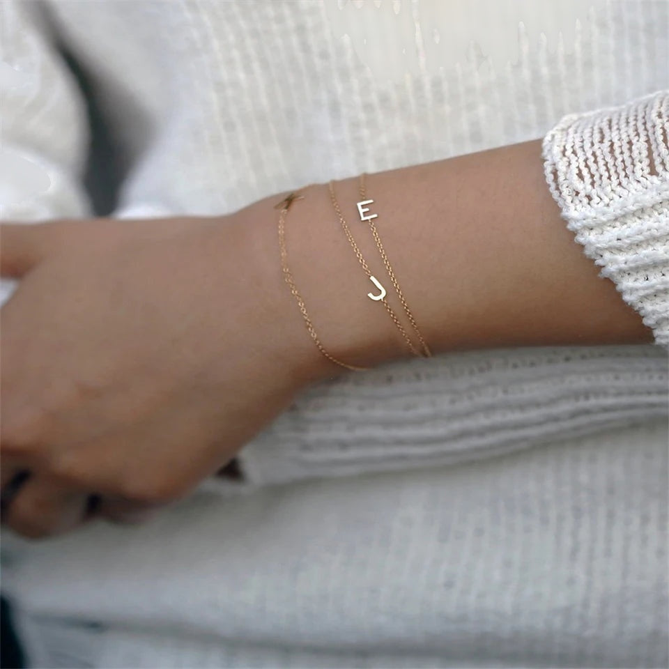 Duas pulseiras com uma inicial dourada no pulso